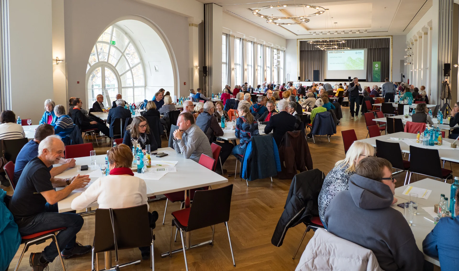 Viele Menschen sitzen an Tischen und unterhalten sich im Kursaal Bad Cannstatt. | © Mick Murphy