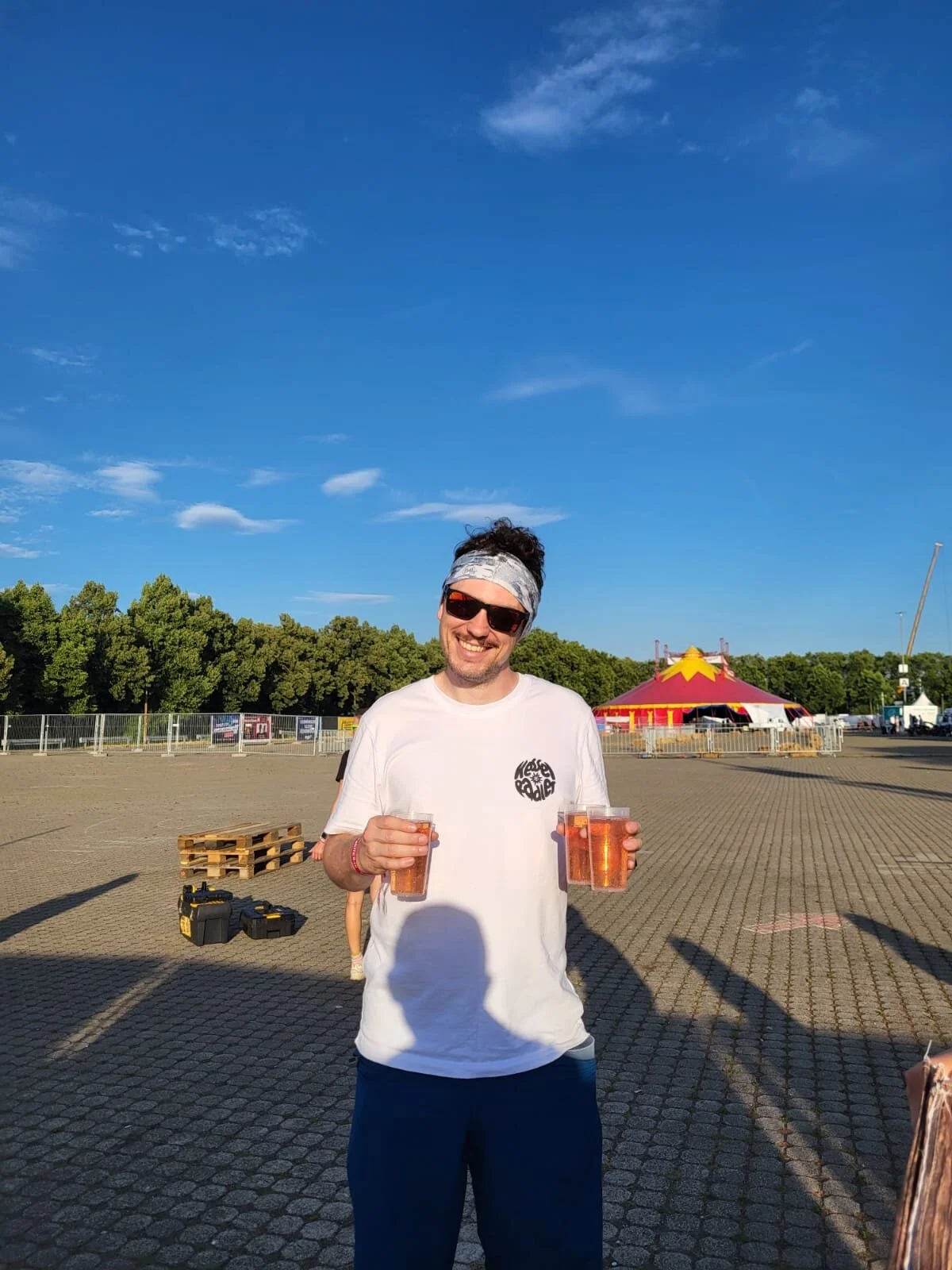 Mann mit weißem T-Shirt hält orangene Getränkebecher in der Hand | © Gabriel Molitor