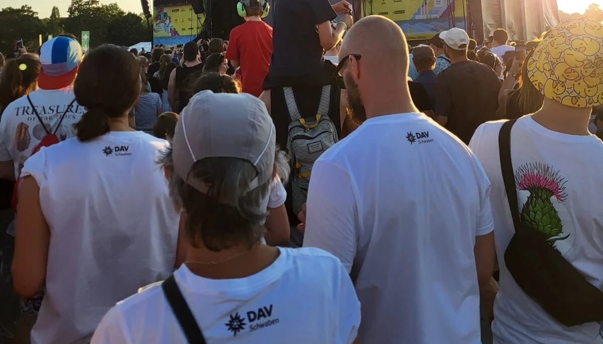 Personen in weißen T-Shirts mit Aufrdruck DAV Schwaben blicken zur Festivalbühne | © Gabriel Molitor