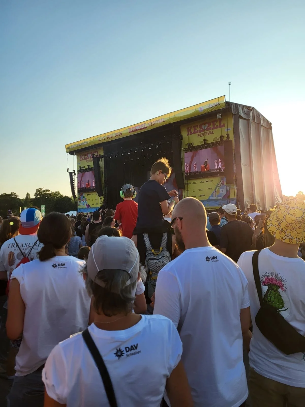 Personen in weißen T-Shirts mit Aufrdruck DAV Schwaben blicken zur Festivalbühne | © Gabriel Molitor