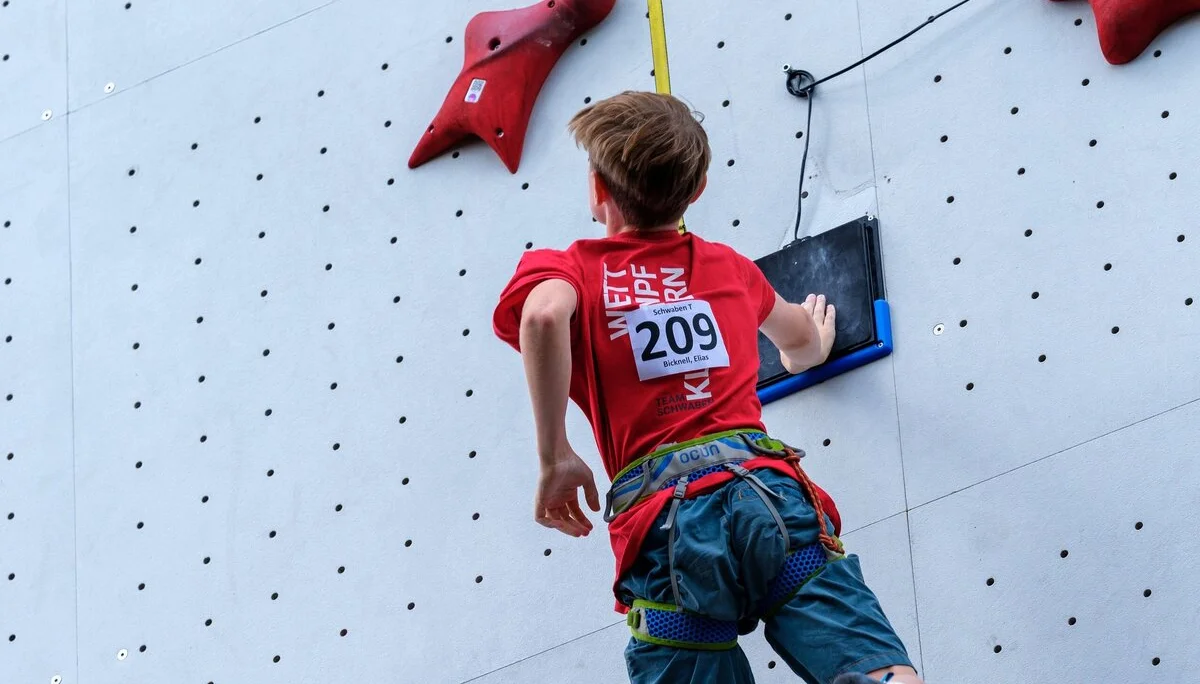 Kletternder Jugendlicher an einer Kletterwand nach dem Abklatschen am Ziel | © Oliver Gobin