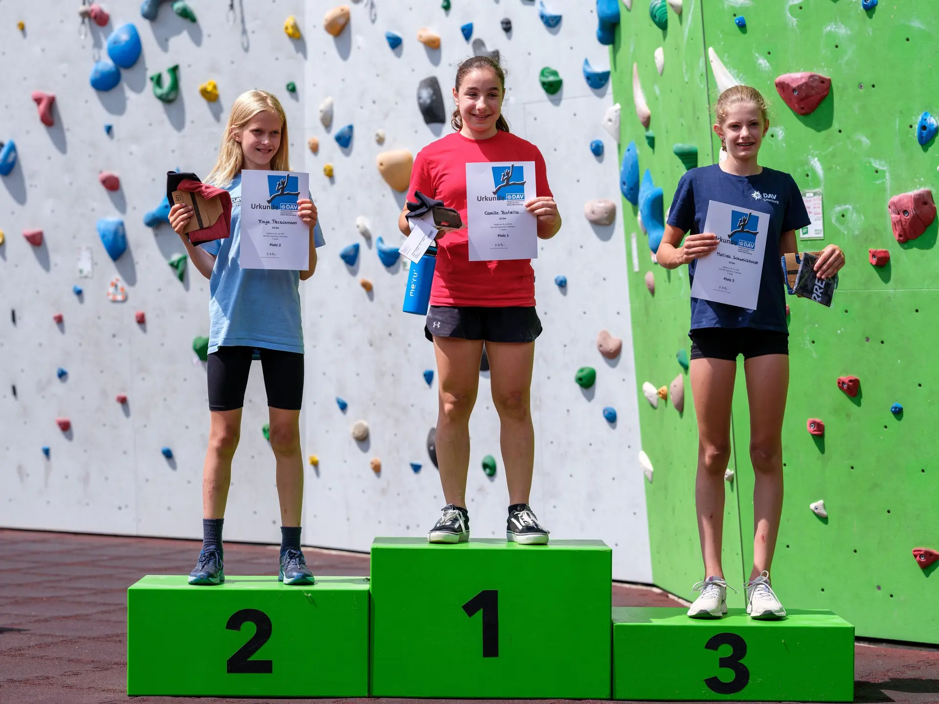 Siegerehrung dreier Mädchen vor einer Kletterwand | © Oliver Gobin