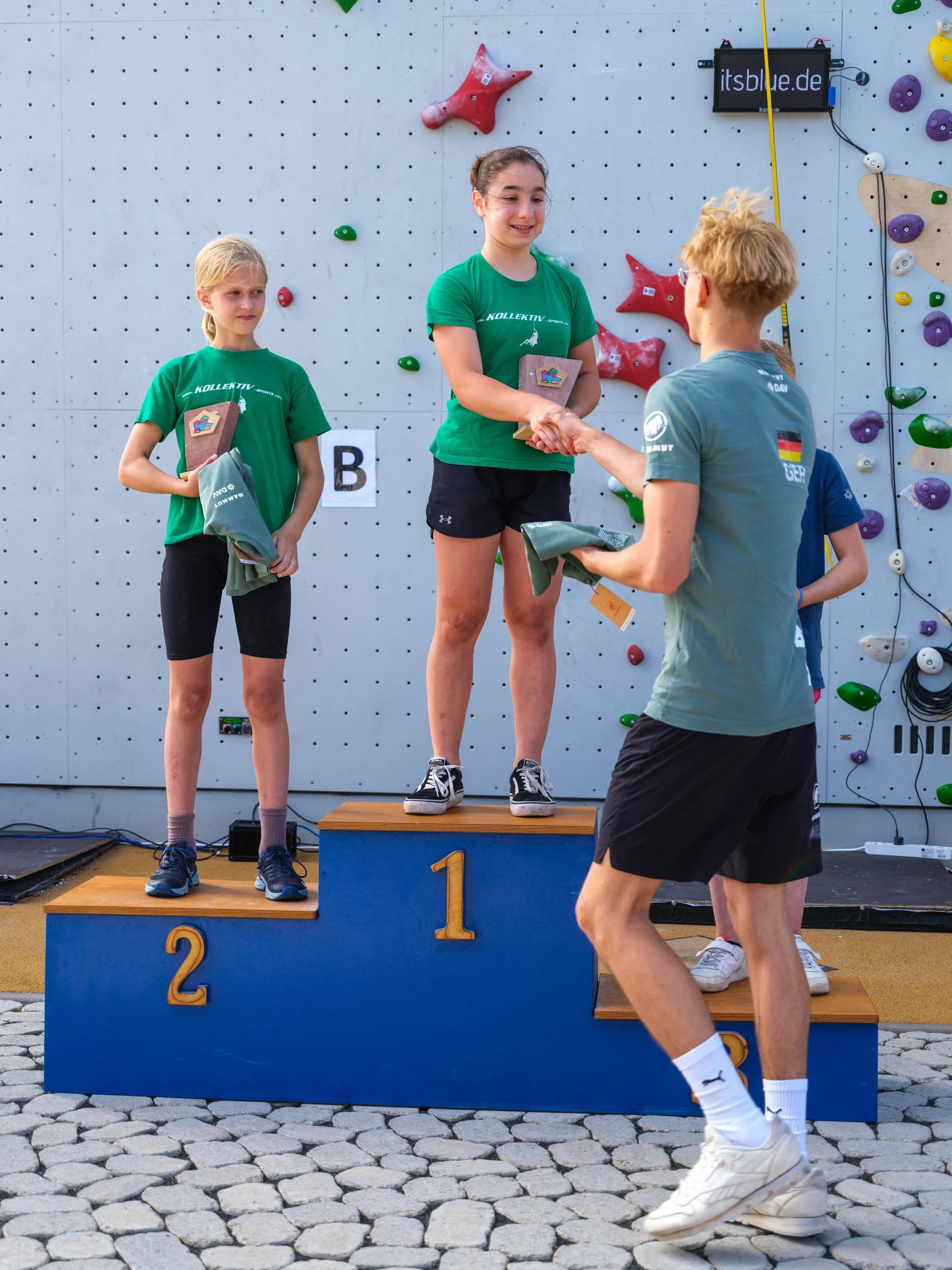 Zwei Mädchen auf einem Podest. Der auf dem ersten Platz wird gratuliert und ein Preis übergeben. | © @oliverclimb / Oliver Gobin