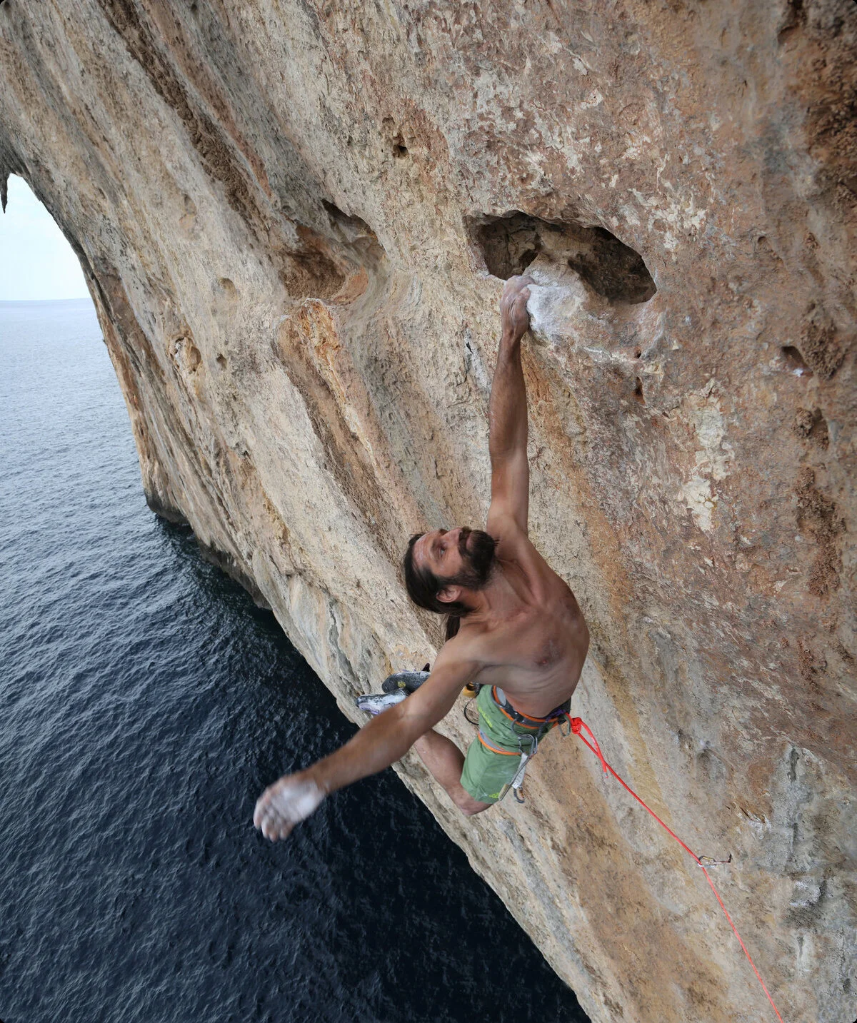 Mann hängt mit der linken Hand am Fels. Er klettert über dem Meer. | © Alexander Huber