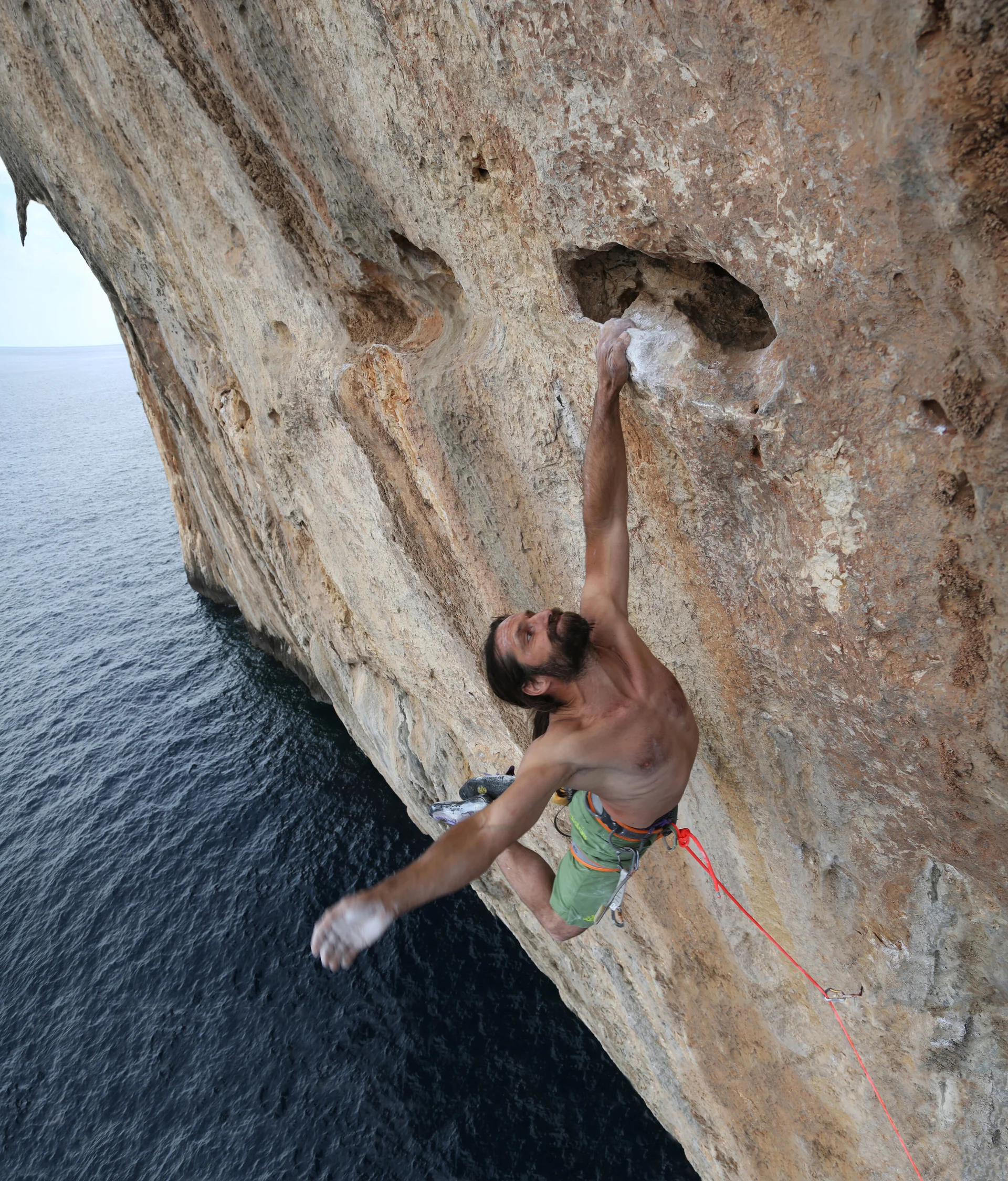 Mann hängt mit der linken Hand am Fels. Er klettert über dem Meer. | © Alexander Huber