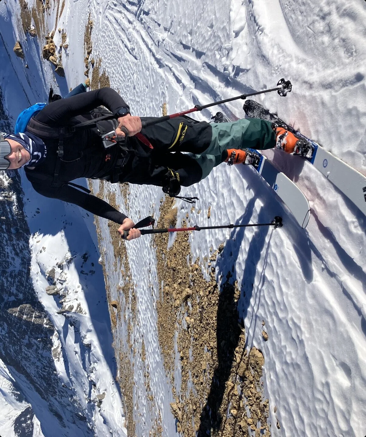 Skitourengeher lächelt in die Kamera während des Aufstiegs, im Hintergrund sieht man Berge | © Fabian Brormann