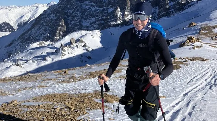 Skitourengeher lächelt in die Kamera während des Aufstiegs, im Hintergrund sieht man Berge | © Fabian Brormann