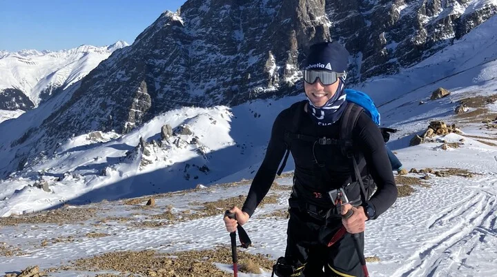 Skitourengeher lächelt in die Kamera während des Aufstiegs, im Hintergrund sieht man Berge | © Fabian Brormann