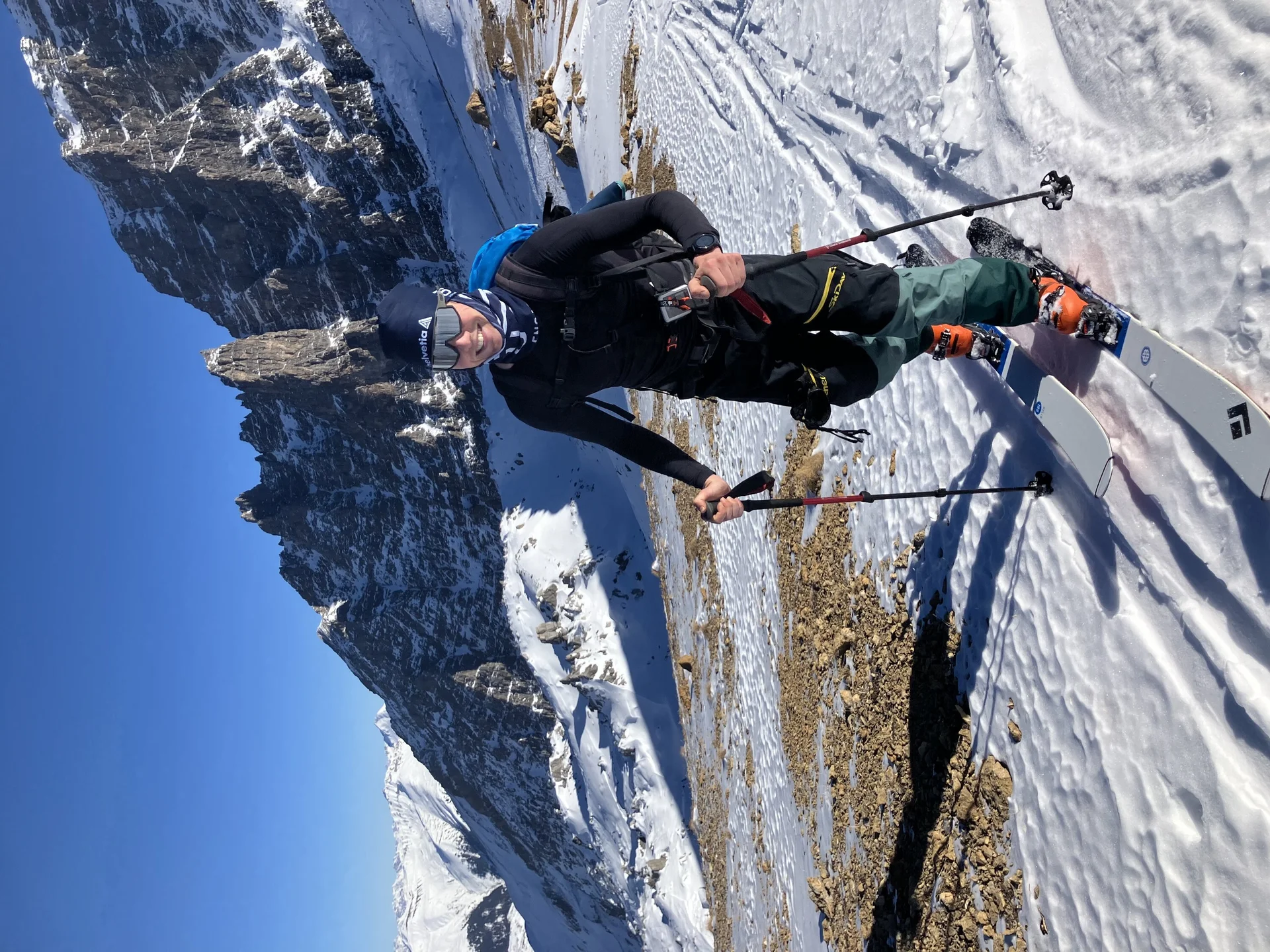 Skitourengeher lächelt in die Kamera während des Aufstiegs, im Hintergrund sieht man Berge | © Fabian Brormann