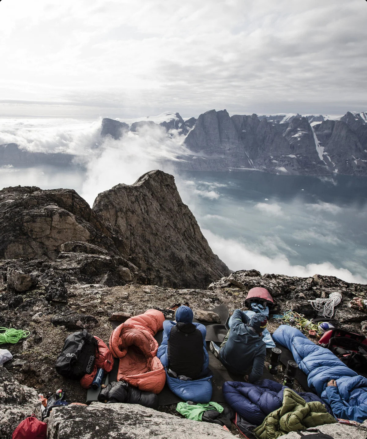 Schlafsäcke auf Felsvorsprung, im Hintergrund Wolken, ein Mann blickt in die Ferne | © © Stefan Glowacz GmbH