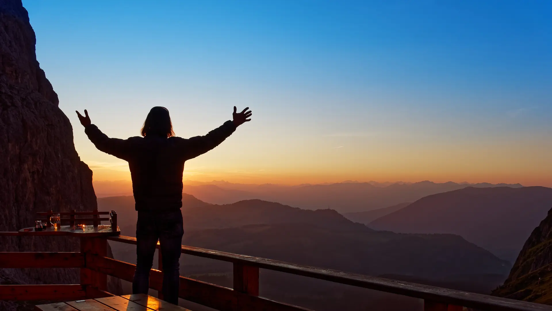 Mensch beim Sonnenaufgang auf der Terrasse einer Berghütte | © Steffen Hoppe, Traum & Abenteuer