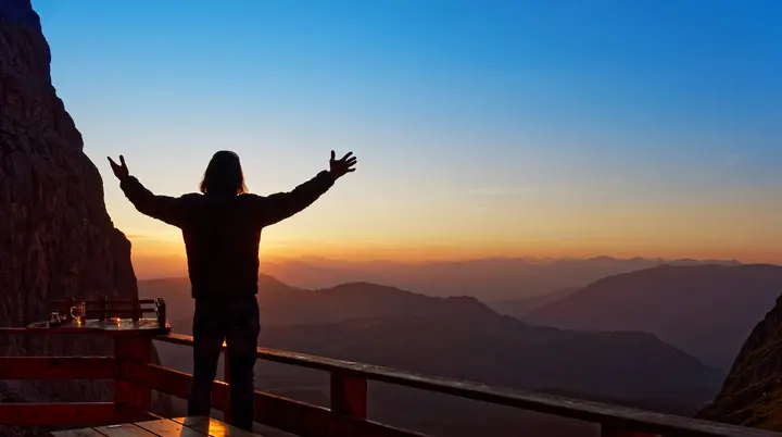 Mensch beim Sonnenaufgang auf der Terrasse einer Berghütte | © Steffen Hoppe, Traum & Abenteuer