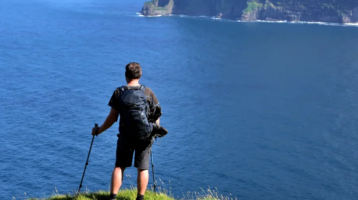 Mann steht auf Klippe und blickt gen Meer. Im Hintergrund ragen begrünte Felsen aus dem Wasser. | © Verena Schmidt