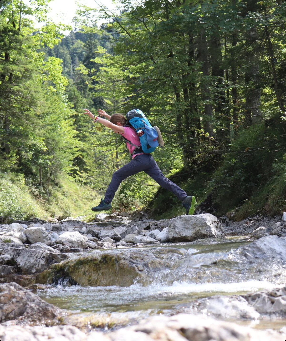 Mädchen quert einen Bach und springt dabei über die Steine, die Hände zeigen in die Höhe. | © Waltraud Zopf