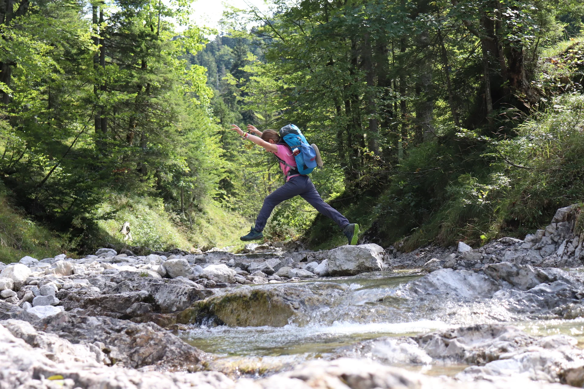 Mädchen quert einen Bach und springt dabei über die Steine, die Hände zeigen in die Höhe. | © Waltraud Zopf