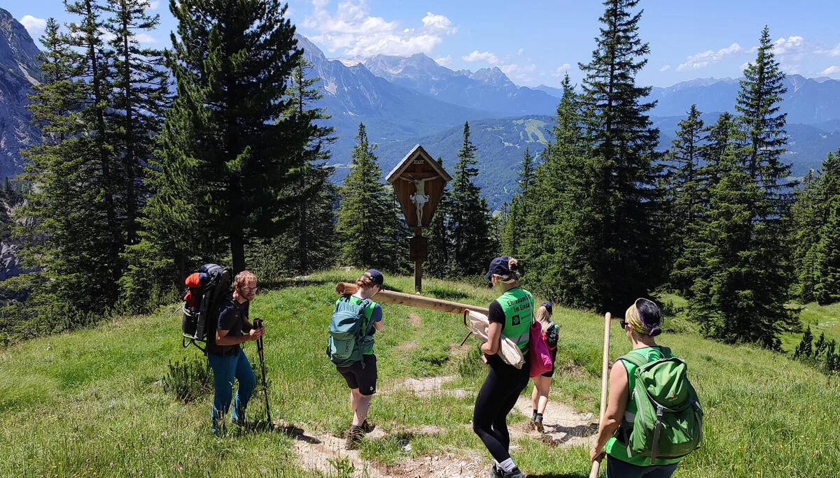 Wegbereitung: Menschen tragen gemeinsam einen Baumstamm über eine Wiese | © DAV
